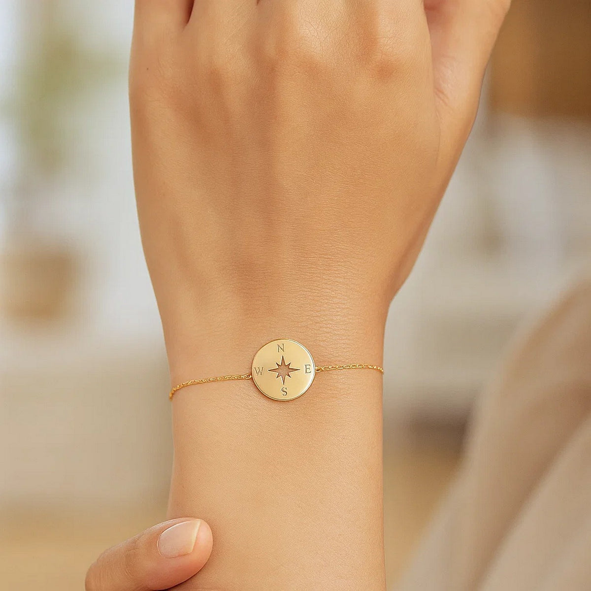 Close-up of 14K gold polished compass charm on delicate yellow gold link bracelet