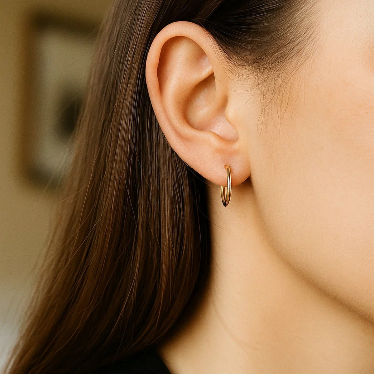 Close-up view of 1.5mm thin 10k yellow gold polished hoop earring in ear