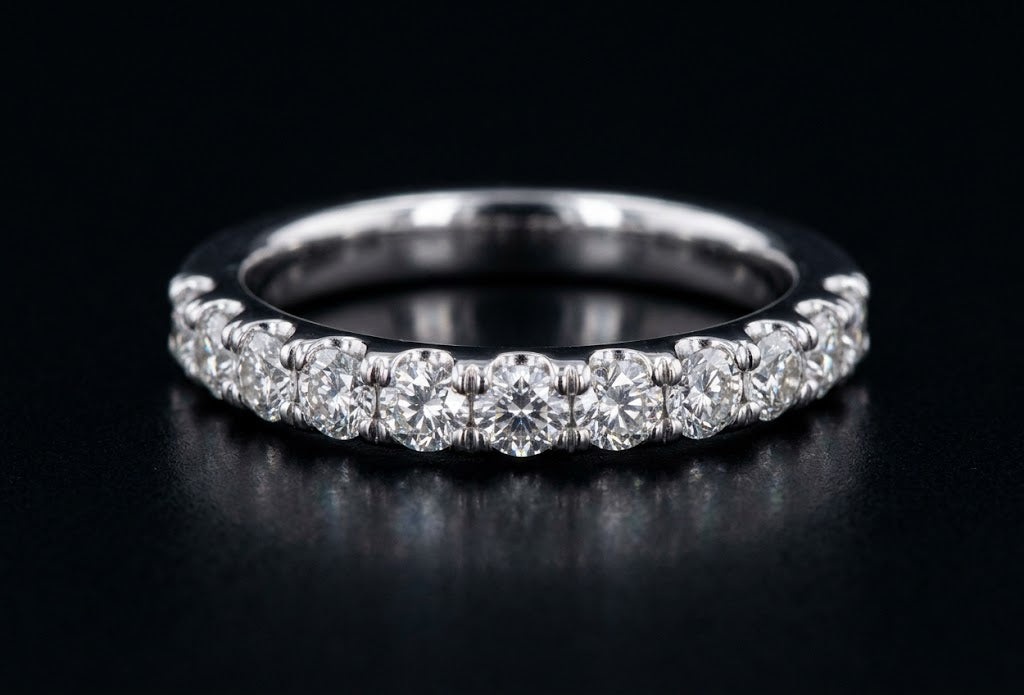 A silver diamond eternity band ring set with round brilliant-cut diamonds, photographed on a reflective black surface.